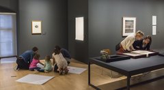Besucher, darunter Kinder, hocken auf dem Boden und zeichnen und betrachten Werke