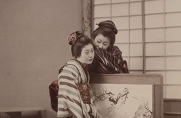 Frau flüstert anderer Frau ins Ohr, beide im Kimono, kleine Stellwand zwischen ihnen