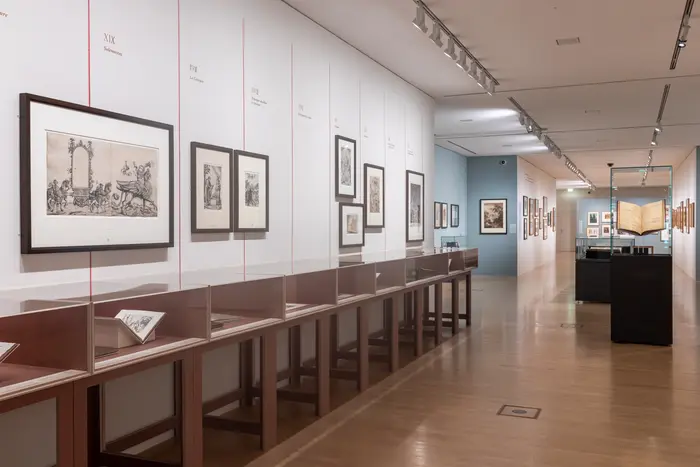 Ein Ausstellungsraum mit Gemälden an den Wänden und Schaukästen aus Glas.