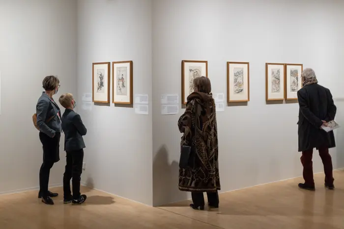 Menschen sehen sich gerahmte Kunstwerke in einem Ausstellungsraum an.