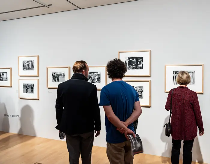 Menschen betrachten Kunstwerke an der Wand eines Ausstellungsraums.