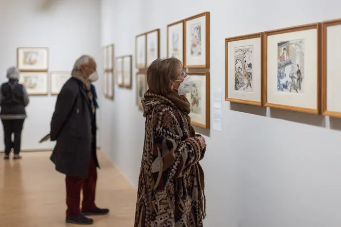 Eine Frau betrachtet gerahmte Zeichnungen in einem Ausstellungsraum.