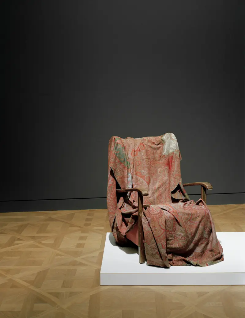 Ein Stuhl steht in einem Ausstellungsraum, und auf dem Stuhl liegen alte Lappen