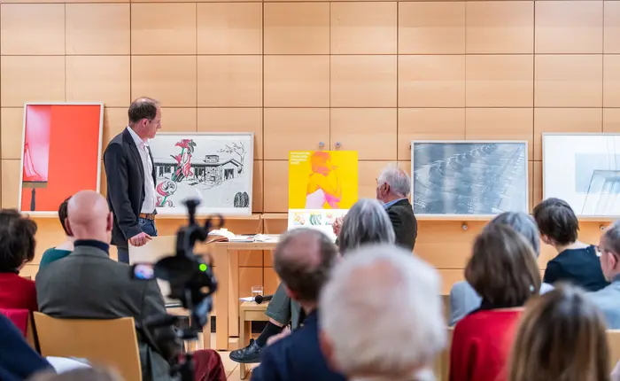 Zwei Männer zeigen auf Kunstwerke, im Vordergrund ist Publikum zu sehen.