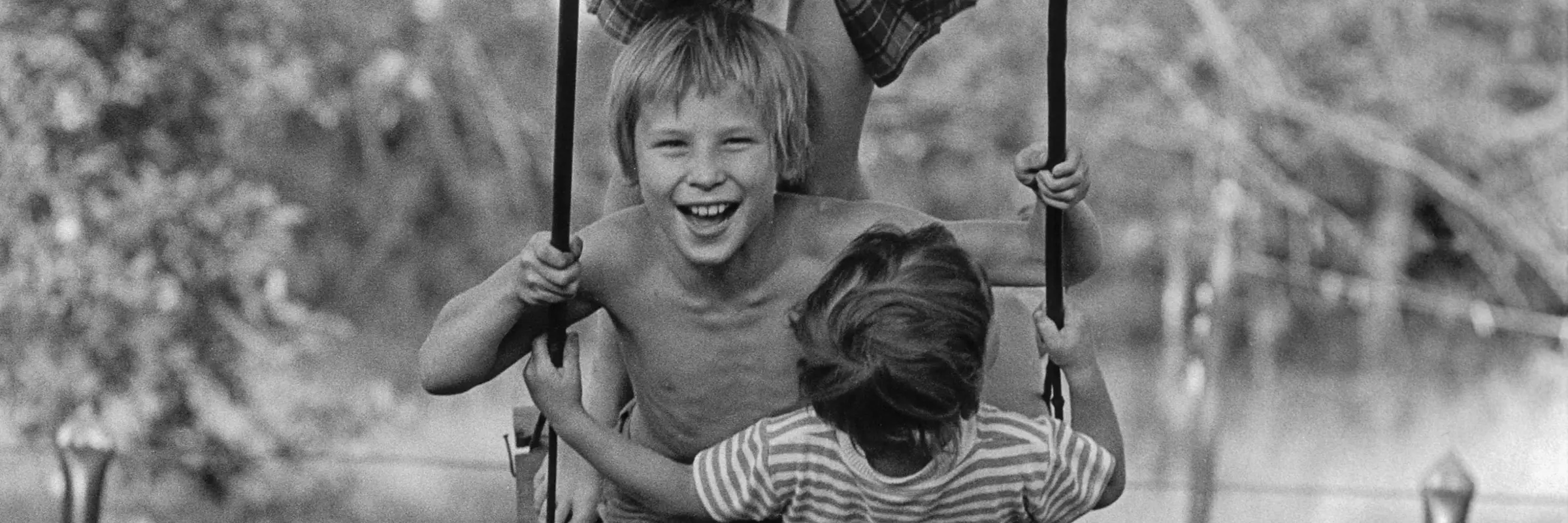 Schwarz-Weiß-Fotografie von drei Kindern auf einer Schaukel