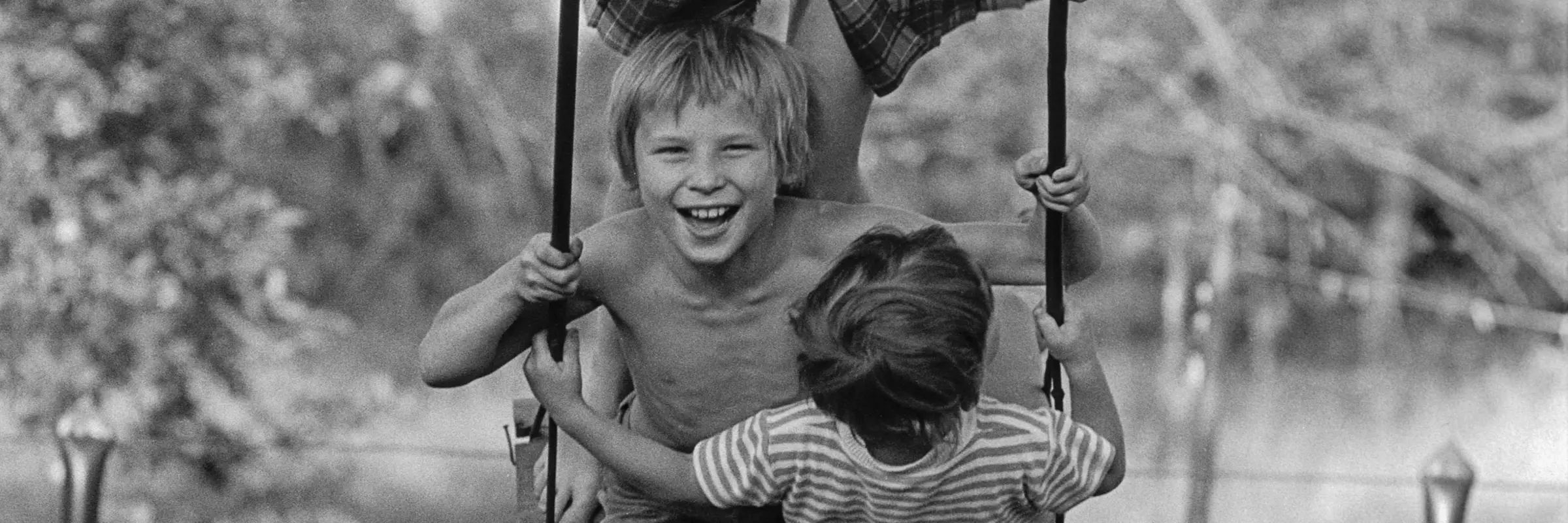 Schwarz-Weiß-Fotografie von drei Kindern auf einer Schaukel