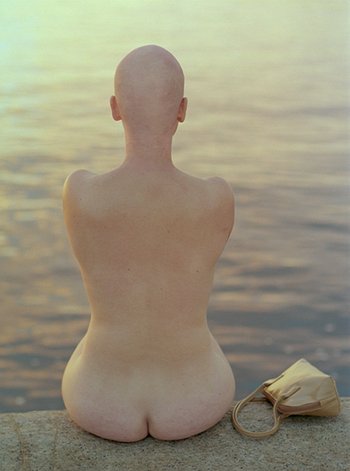 Rückenansicht einer nackten Frau ohne Haare vor Wasser