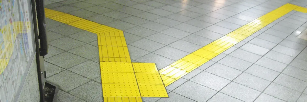 Gelbe, mit linienförmigen Erhebungen bedeckte Fliesen heben sich als Abzweigung von einem grauen Fliesenboden ab.