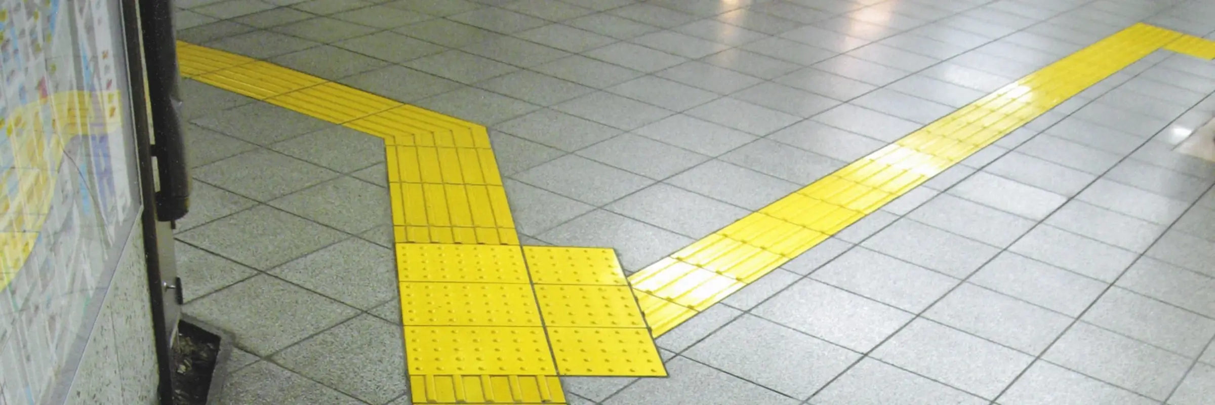 Gelbe, mit linienförmigen Erhebungen bedeckte Fliesen heben sich als Abzweigung von einem grauen Fliesenboden ab.