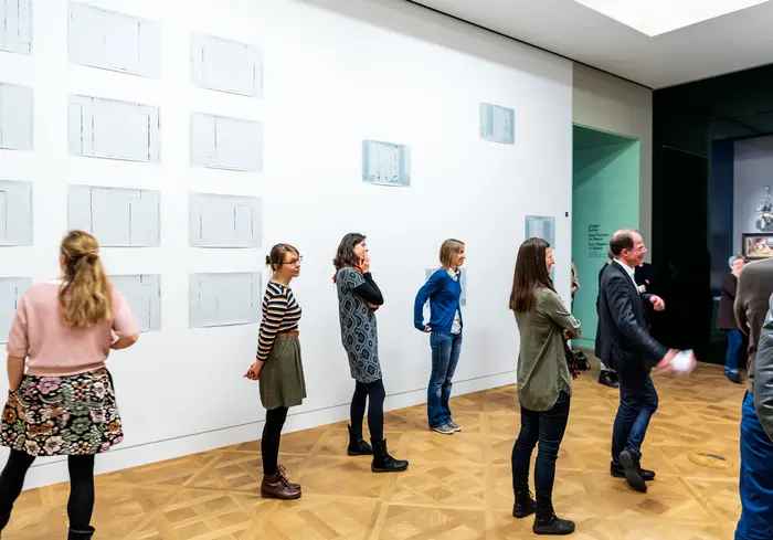 Menschen stehen in einem Ausstellungsraum mit weißen Wänden und Holzboden.