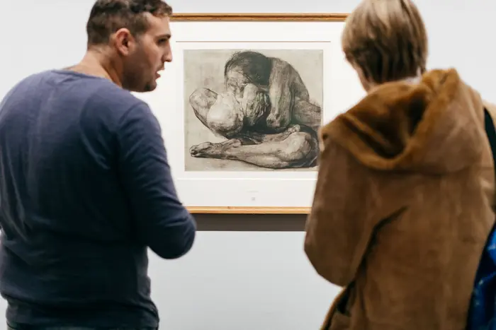 Zwei Besucher besprechen eine Druckgraphik von Käthe Kollwitz.