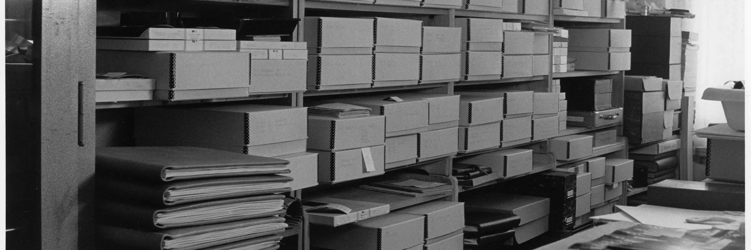 Schwarz-Weiß-Fotografie eines Regals mit Boxen und Mappen.