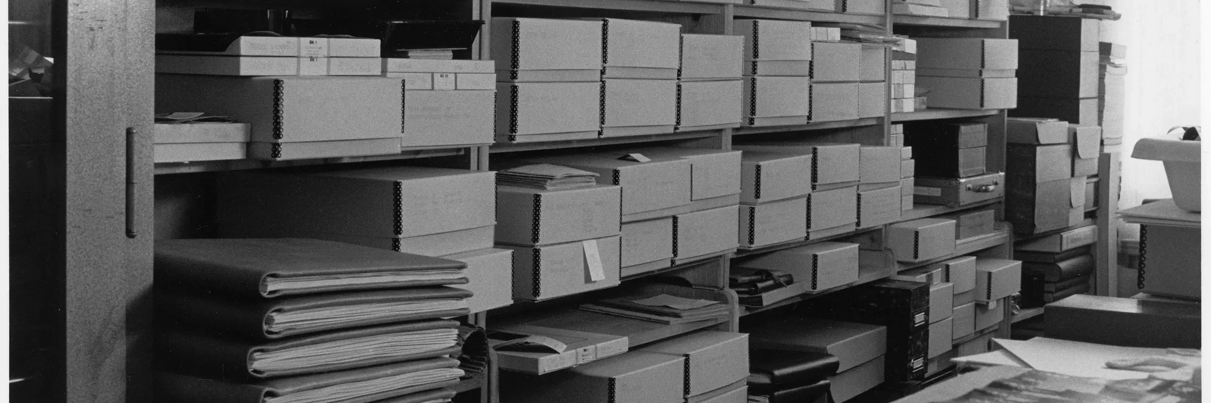 Schwarz-Weiß-Fotografie eines Regals mit Boxen und Mappen.