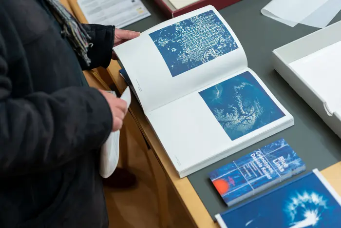 Eine Person blättert in einem Buch, das Abbildungen von blauen Kunstwerken zeigt.