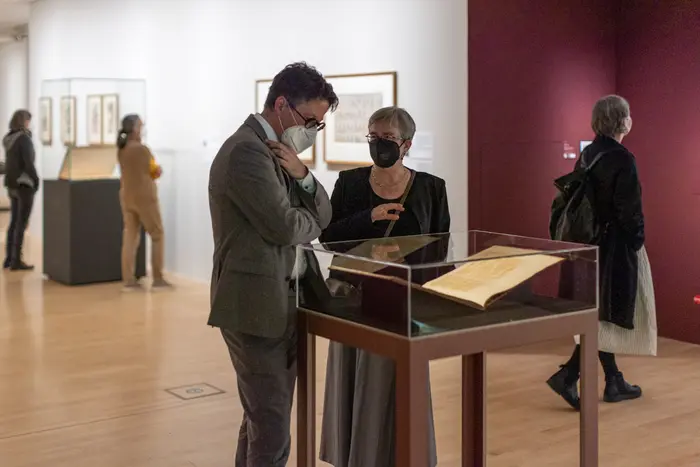 Personen betrachten ein aufgeschlagenes Buch in einem gläsernen Schaukasten.