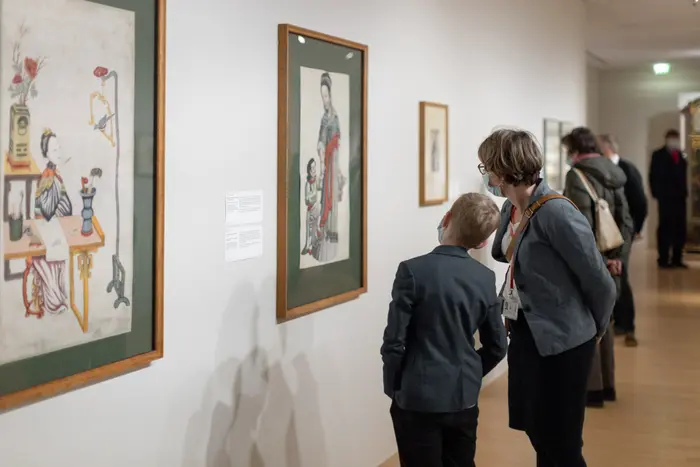 Besucher betrachten ein gerahmtes Kunstwerk in einem Ausstellungsraum.