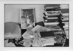 Schwarz-Weiß-Fotografie eines Schreibtisches mit Büchern und Fotos