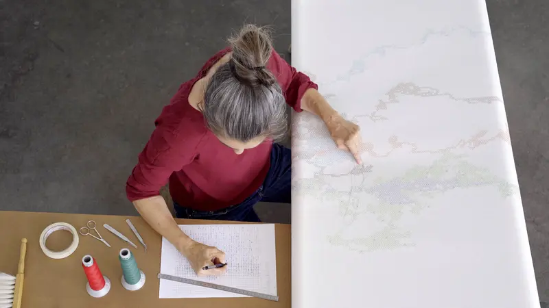 Eine Frau arbeitet an einem Kunstwerk auf weißem Untergrund.