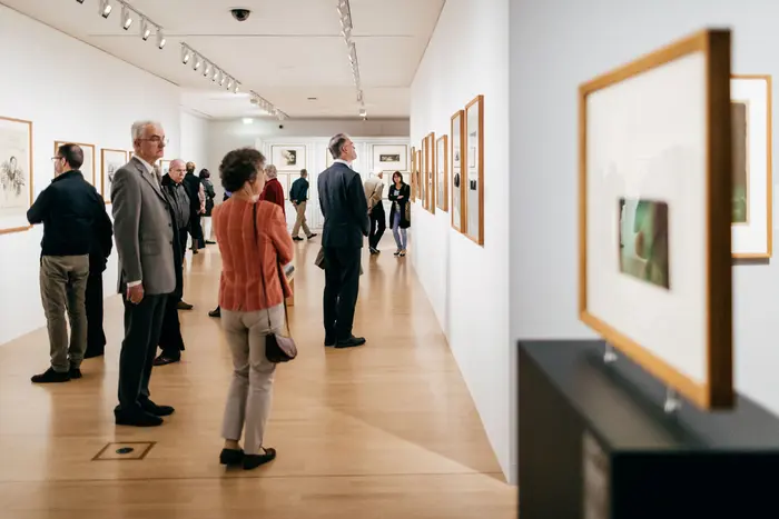 Ein Haufen von Besuchenden in einem langen Ausstellungsraum schaut sich Grafiken an