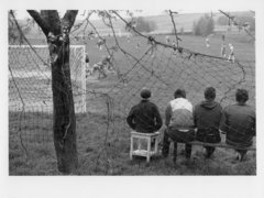 Schwarz-Weiß-Fotografie von vier Männern, die vor einem Fußballfeld sitzen
