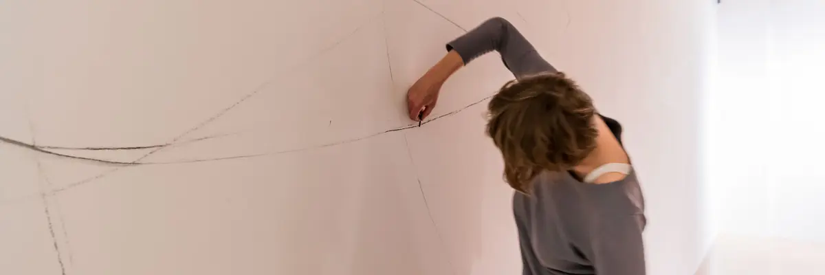 Eine Person malt dünne Linien an eine weiße Wand.