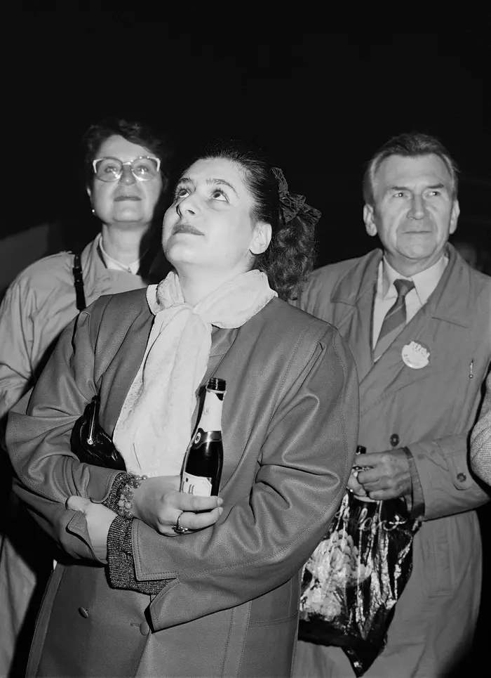 Die Schwarz-Weiß-Fotografie dreier Menschen, eine hält eine Flasche.