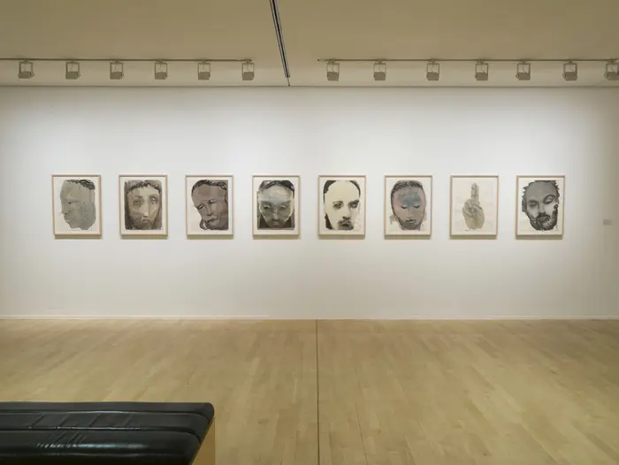 Eine Reihe gerahmter Gemälde hängen an einer weißen Wand in einem Ausstellungsraum.