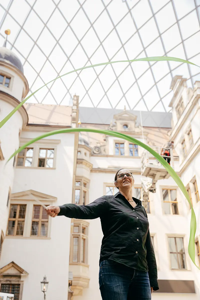 Eine Frau schwenkt eine dünne, grüne Stoffbahn im kleinen Schlosshof des Residenzschlosses.