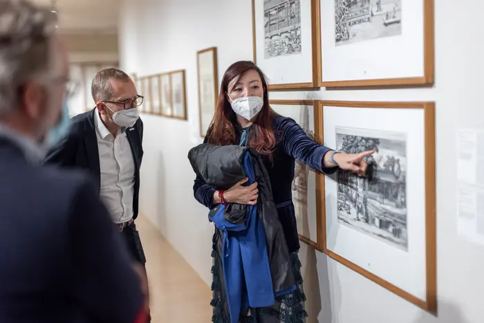 Eine Frau weist mit dem Finger auf Details einer gerahmten Zeichnung.