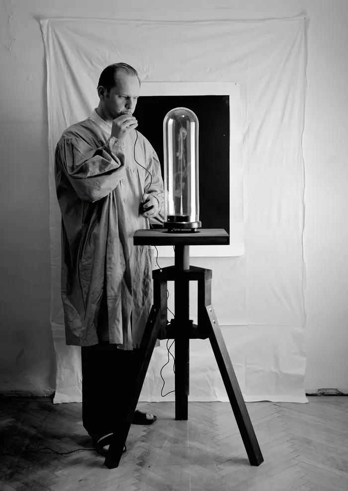 Mann steht neben einer länglichen Glasglocke und bläst etwas hinein