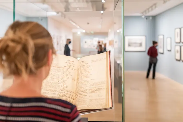 Eine Person betrachtet ein aufgeschlagenes Buch in einem Glasschaukasten.
