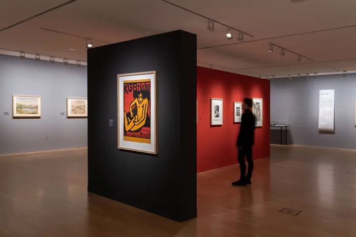 Ein Ausstellungsraum mit Gemälden und Zeichnungen an bunten Wänden.