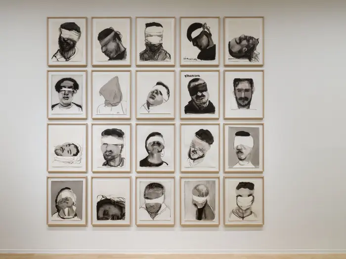 In einem Quadrat angeordnet hängen Porträtzeichnungen an einer weißen Wand.