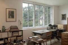 Raum mit Schreibtisch, Büchern, Malutensilien und großem Fenster