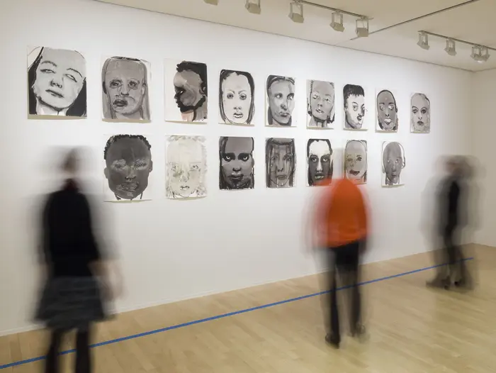 Personen vor einer Wand, an der Porträtzeichnungen hängen.