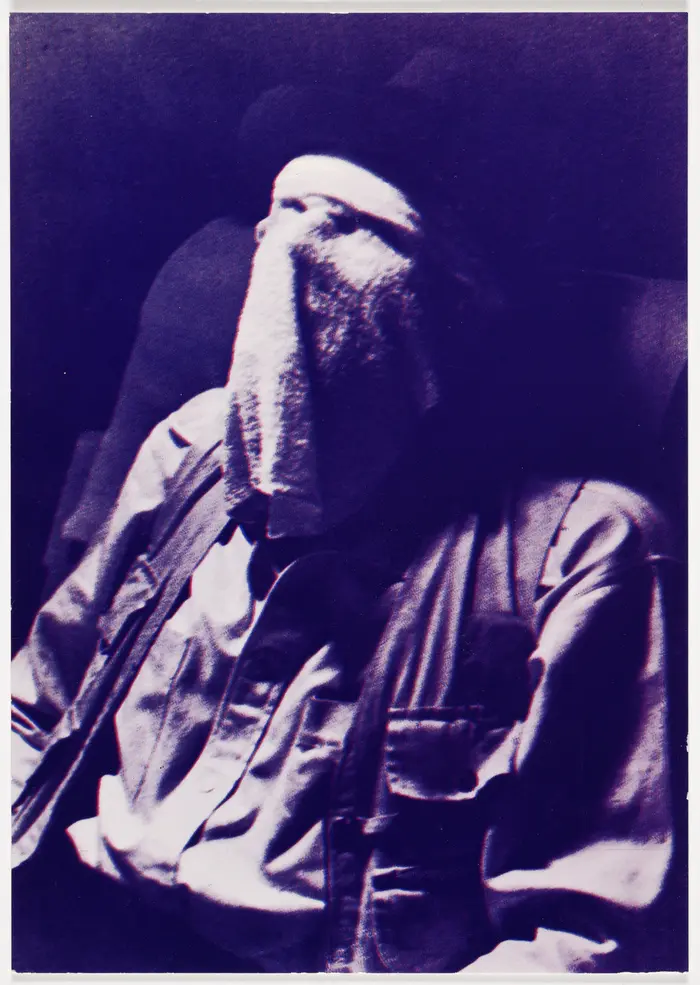 Die Schwarz-Weiß-Fotografie einer sitzenden Person, deren Gesicht mit einem Tuch bedeckt ist.