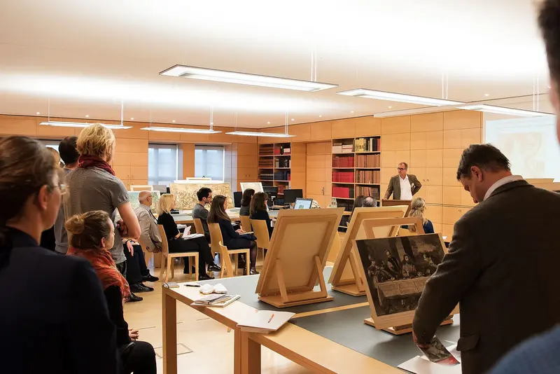 Besucherinnen und Besucher stehen im Studiensaal und hören einen Vortrag an