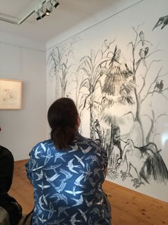 Frau / Besucherin sitzt vor Ausstellungsimpression, Wandbild „Alle Vögel sind schon da“